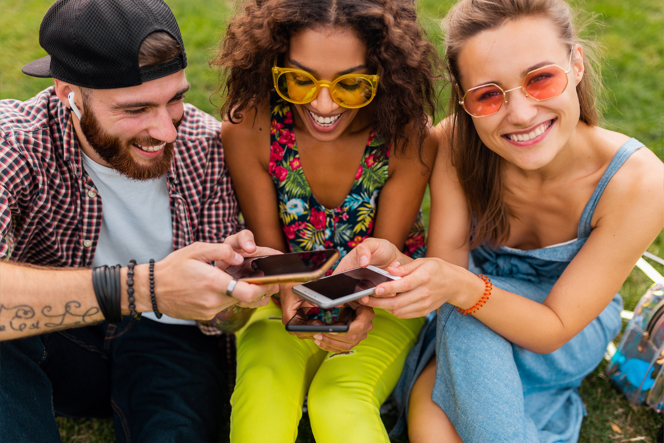 Three young gamers - one man and two women - looking at their mobile phones so they won't miss the next summer game event in our mobile games.