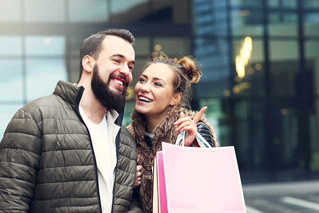 Couple souriant avec sacs de shopping devant un centre commercial, Black Friday