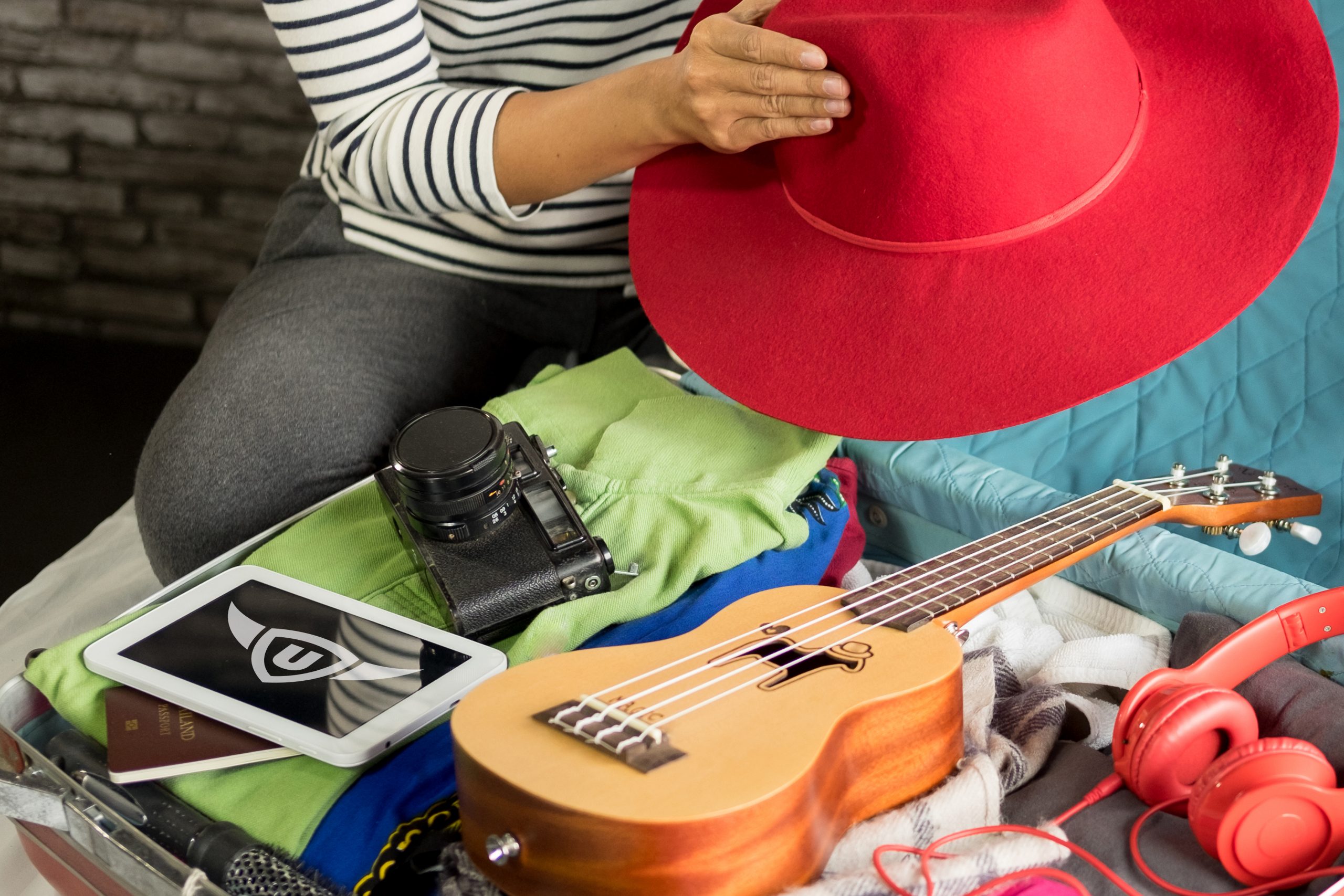 Eine Frau packt ihren Koffer und nimmt eine Ukulele sowie ein Tablet mit upjers Games mit