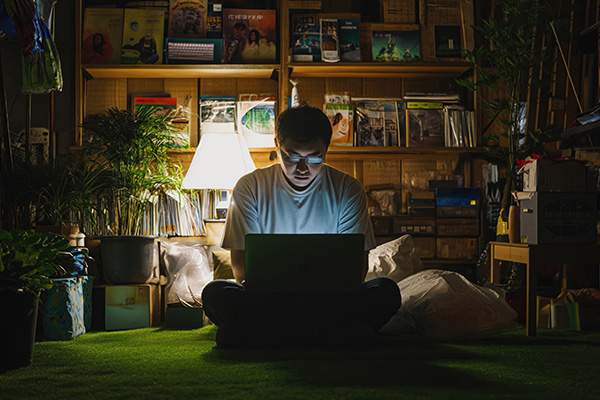 Ein junger Mann sitzt mit Laptop im Zimmer und genießt Edutainment Spiele, um dabei viel über Tiere, Natur, Dinos oder Geschichte zu lernen.