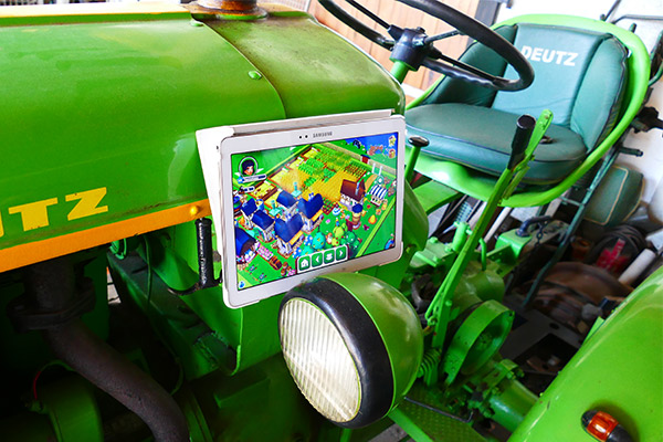Auf einem grünen alten Traktor steht ein Tablet, wo gerade eins unserer kostenlosen Farm Spiele "My Free Farm 2" läuft.